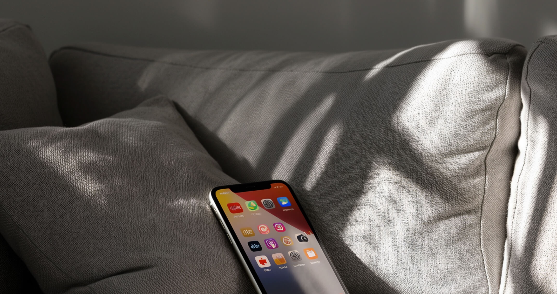 Smartphone resting on a gray couch cushion with sunlight casting shadows on the fabric.