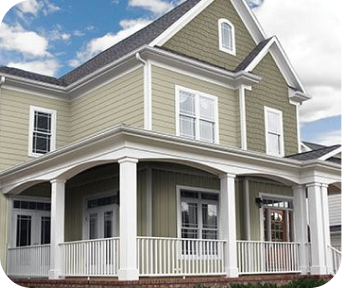Large two-story green house with white trim, multiple windows, and a spacious wraparound porch under blue sky with clouds.