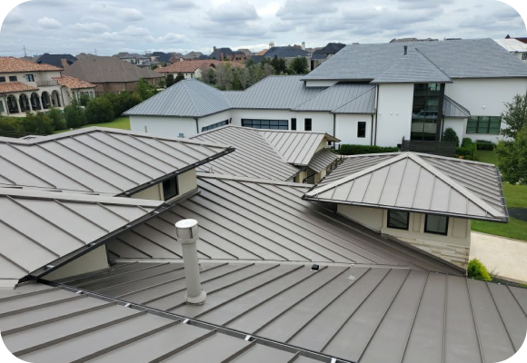 View of multiple connected modern metal rooftops with a cloudy sky and residential homes in the background.