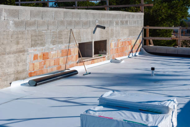 Flat rooftop with white waterproof membrane installation in progress and building materials placed on top near a concrete wall.