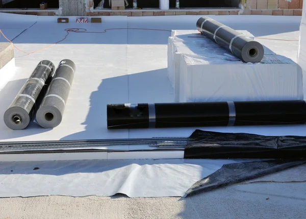Construction site with rolls of black waterproofing membrane and white insulation material on a concrete surface.