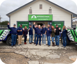 Team of ten people standing in front of a Springtree Restoration building, smiling and waving.