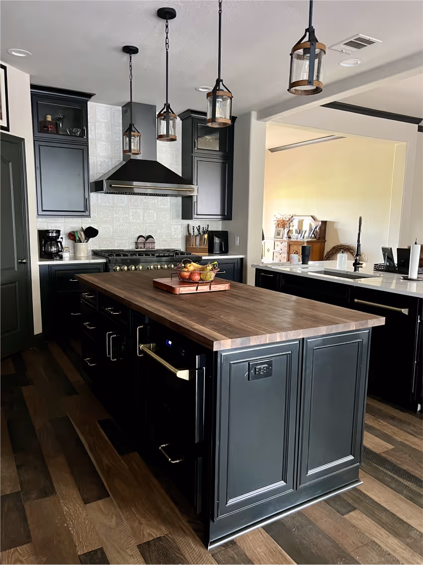 Modern kitchen with dark cabinets, wooden island countertop, stainless steel stove, hanging lantern-style lights, and hardwood floor.