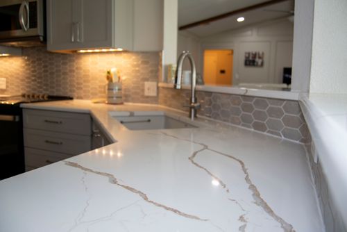 Modern kitchen with white marble countertop featuring gray and brown veining, hexagonal tile backsplash, and stainless steel faucet.