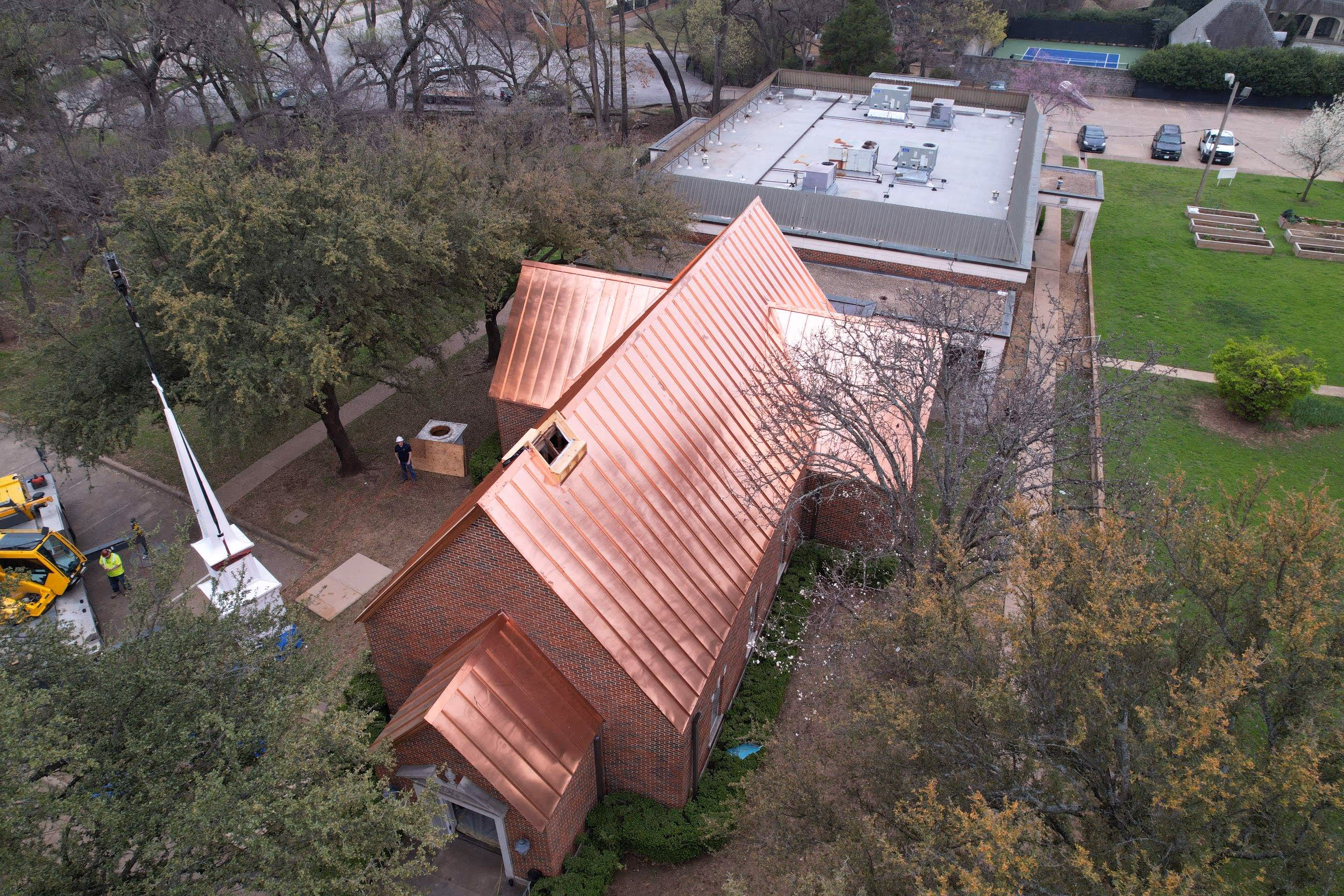 Aerial view of a brick building with a shiny copper roof surrounded by trees and greenery.