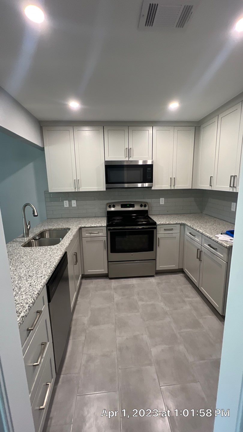 Modern U-shaped kitchen with gray tiled floor, white cabinets, granite countertops, stainless steel sink, dishwasher, electric stove, and microwave above the stove.