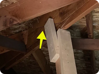 Close-up of attic wooden beams and rafters with a yellow arrow pointing at a connection joint.