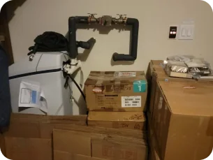 Utility room with a water heater, black pipes with valves, and several stacked cardboard boxes.
