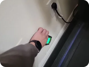 Person's hand pressing a glowing green button mounted on a wall near a treadmill and electrical outlet.