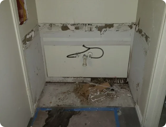 Empty utility space with exposed plumbing and dirty floor with debris, surrounded by partially stripped walls.