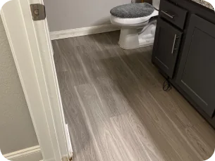 Bathroom with wood-patterned vinyl flooring, a white toilet with a gray seat cover, and dark gray cabinets with silver handles.