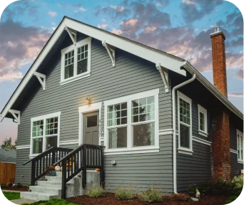 Gray wooden house with white trim, a small front porch, and a brick chimney under a blue sky with clouds.