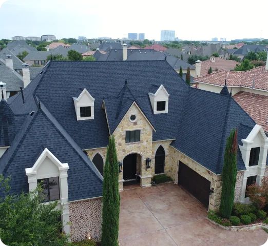 Stone and brick house with steep dark gray roof and two tall cypress trees at the front driveway.