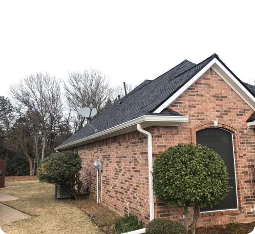 Side view of a brick house with a satellite dish on the roof and neatly trimmed round bushes near the wall.