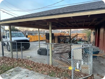 Open garage or carport with a chain-link fence gate, a white truck parked inside, and various tools and equipment scattered around.