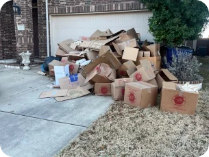 Large pile of flattened and stacked cardboard boxes outside a garage in a residential driveway.