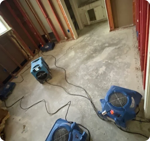 Empty room with stripped walls and four blue floor fans used for drying the concrete floor.