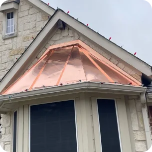Copper roof over bay windows on a stone house under an overcast sky.