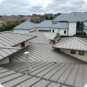 View of multiple modern metal rooftops with an overcast sky and distant houses in the background.