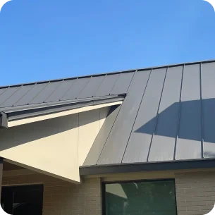 Modern house roof with dark gray metal panels under a clear blue sky.