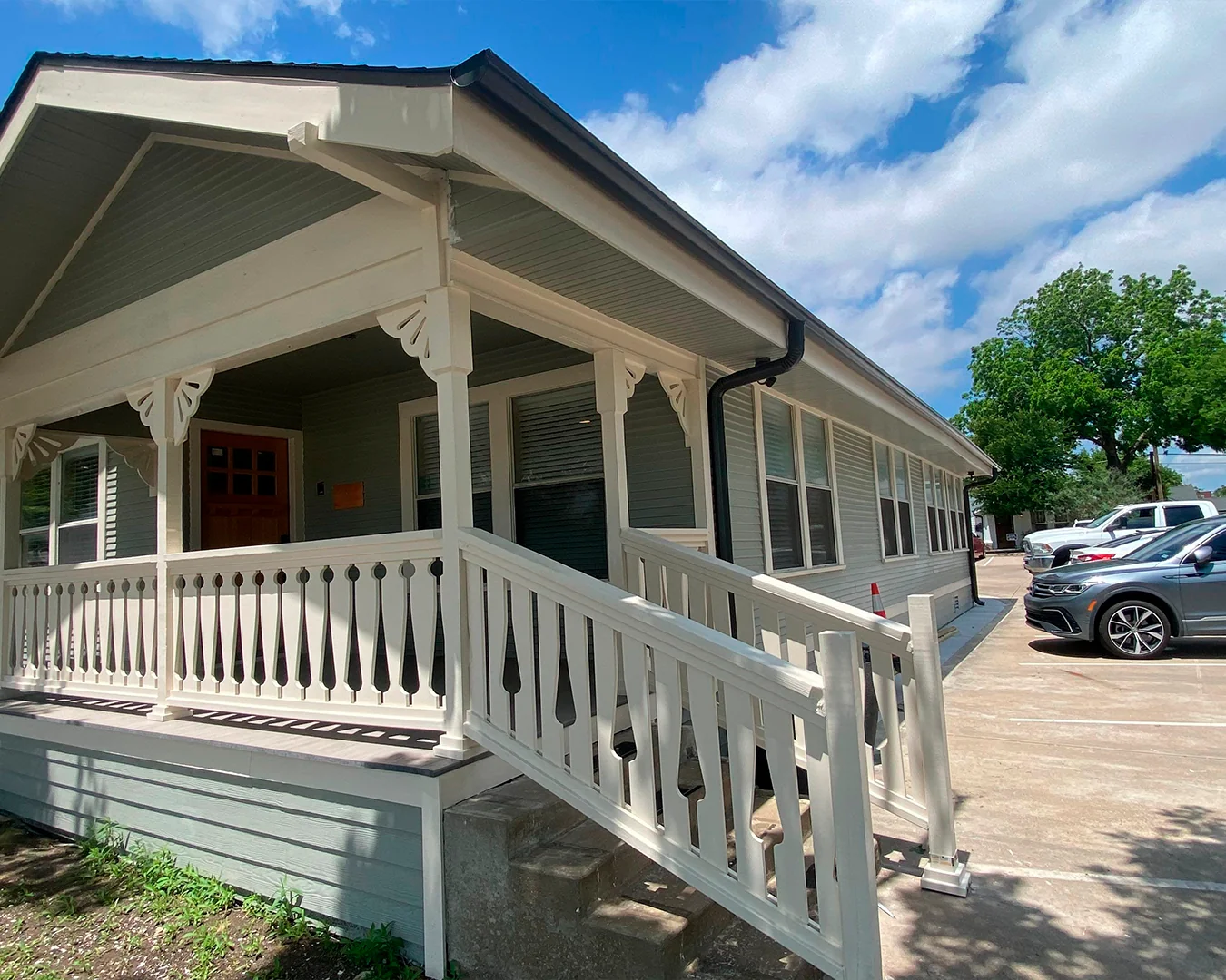 Single-story house with a light green exterior, white decorative railing, and a wheelchair ramp next to concrete steps under a blue sky.
