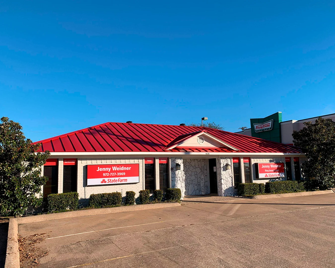 Single-story white stone building with a red roof and State Farm insurance signs for Jenny Weidner, adjacent to a Krispy Kreme store.