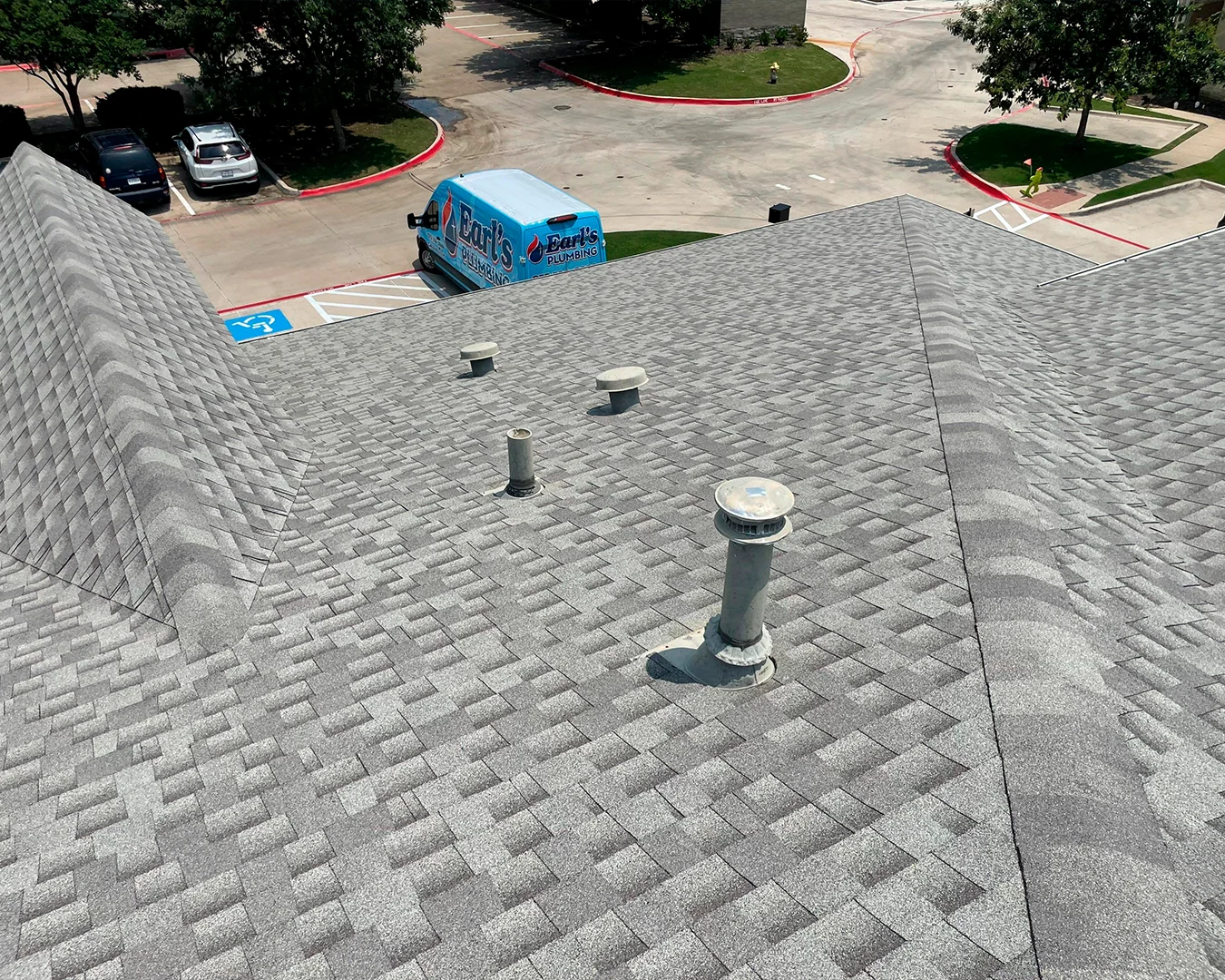 Gray shingled rooftop with multiple vent pipes and an Earl's Plumbing van parked in a parking lot below.