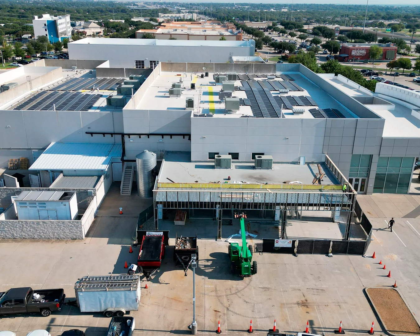 Aerial view of a commercial building with solar panels on the roof and construction work with machinery in the parking lot.