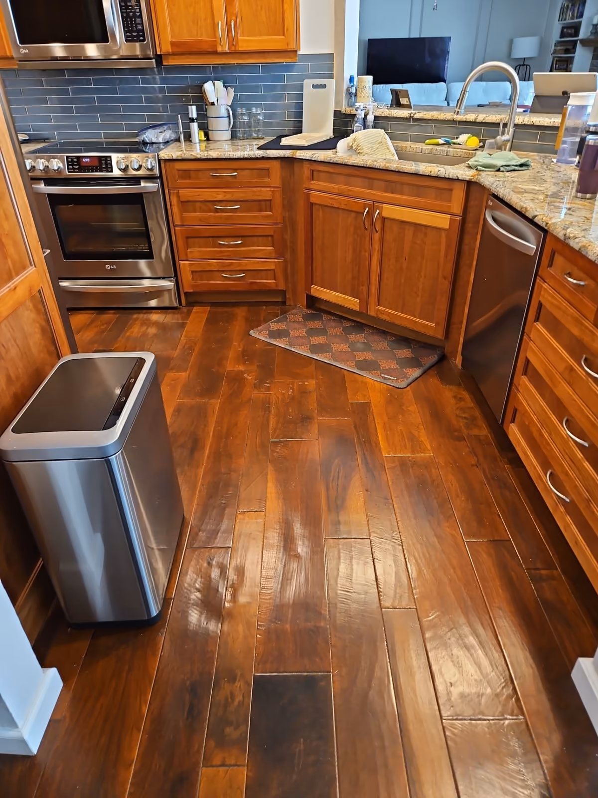 Kitchen with wooden floor, wooden cabinets, stainless steel oven, dishwasher, and a trash bin.