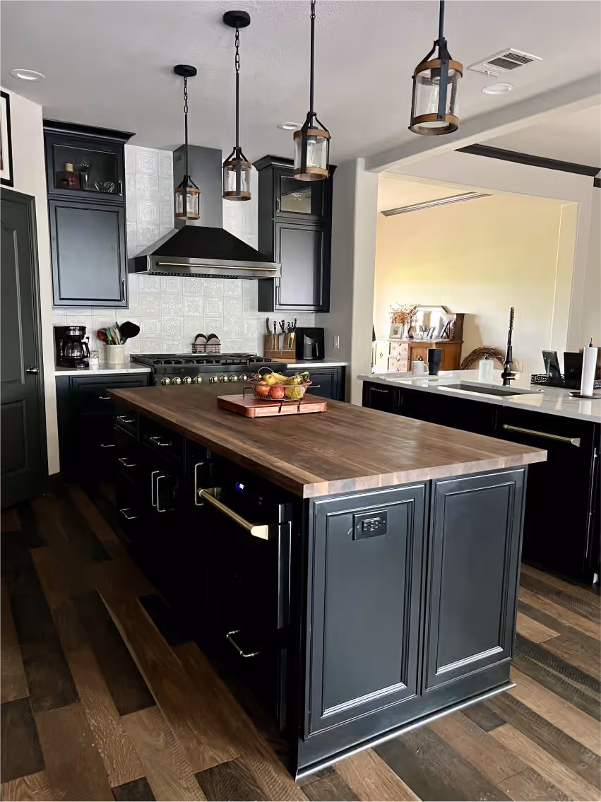 Modern kitchen with dark cabinets, wooden island countertop, stainless steel stove, hanging lantern-style lights, and hardwood floor.