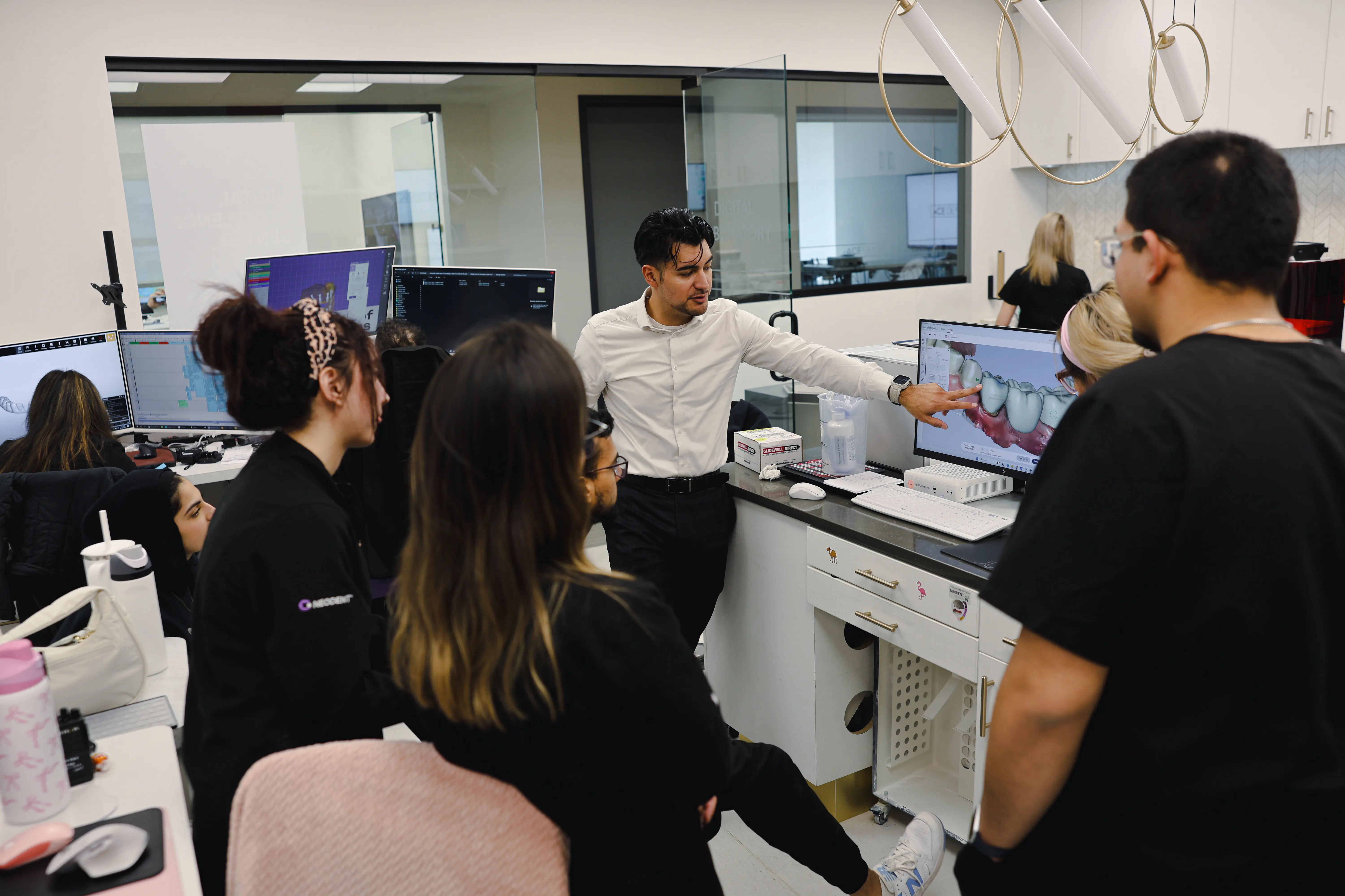 Group of dental professionals gathered around a computer displaying a 3D dental model while a man in a white shirt explains.