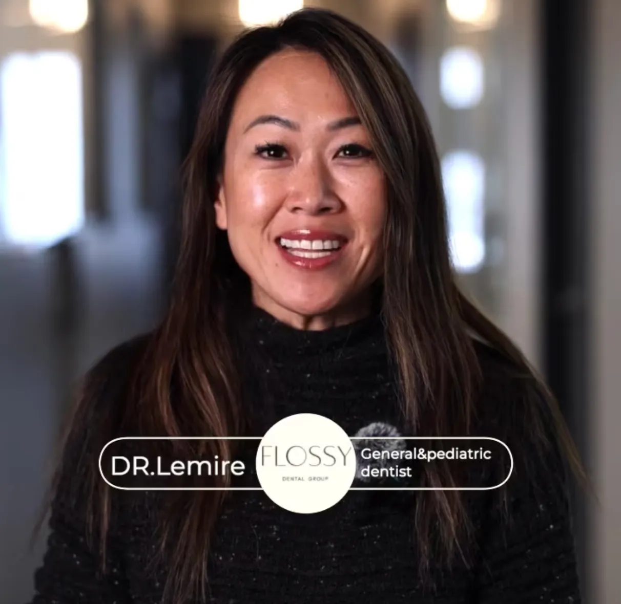 Smiling woman with long dark hair wearing a black sweater, labeled as Dr. Lemire, General and Pediatric Dentist at Flossy Dental Group.