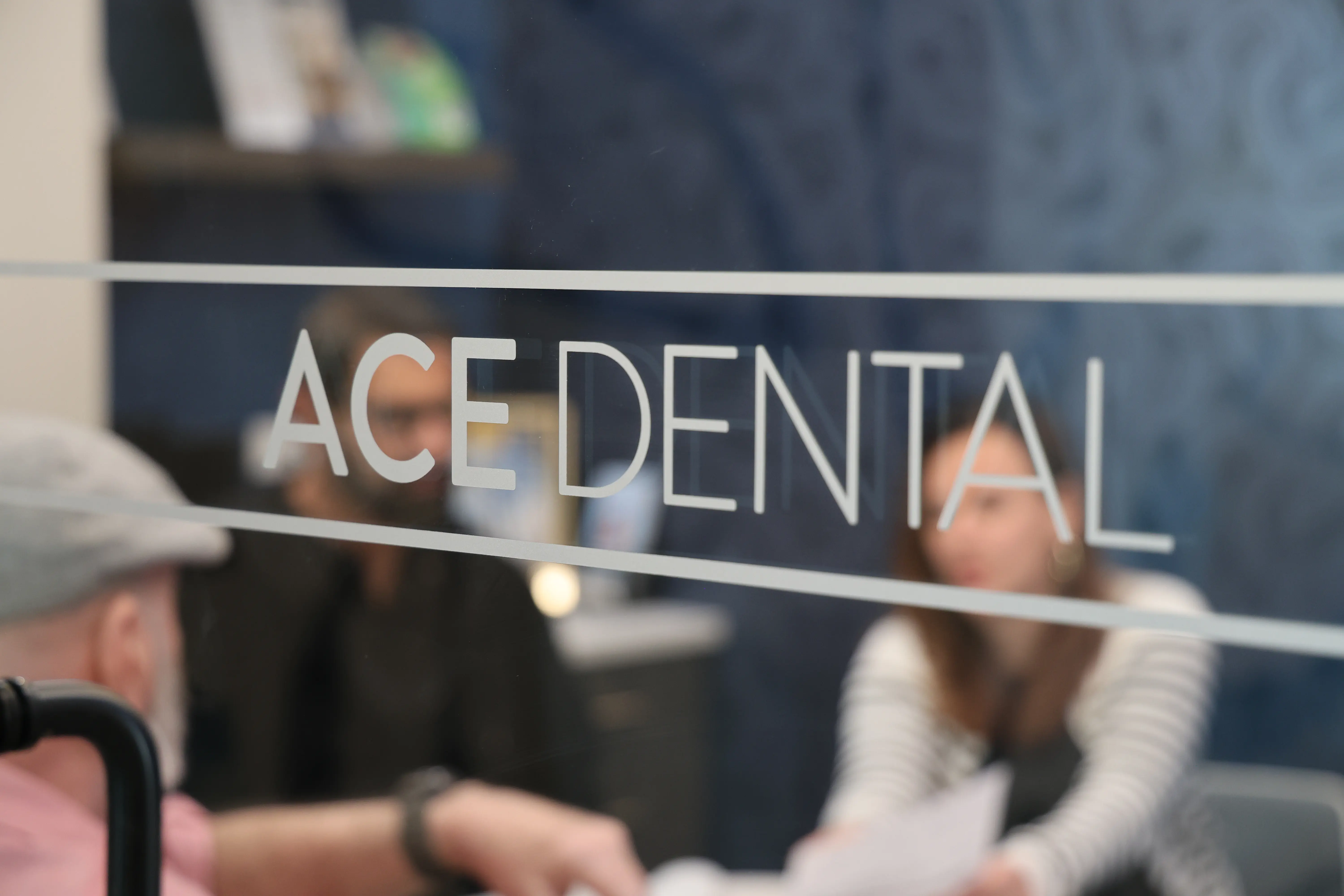 Frosted glass door with the text 'ACE DENTAL' and blurred background of people in a dental office.