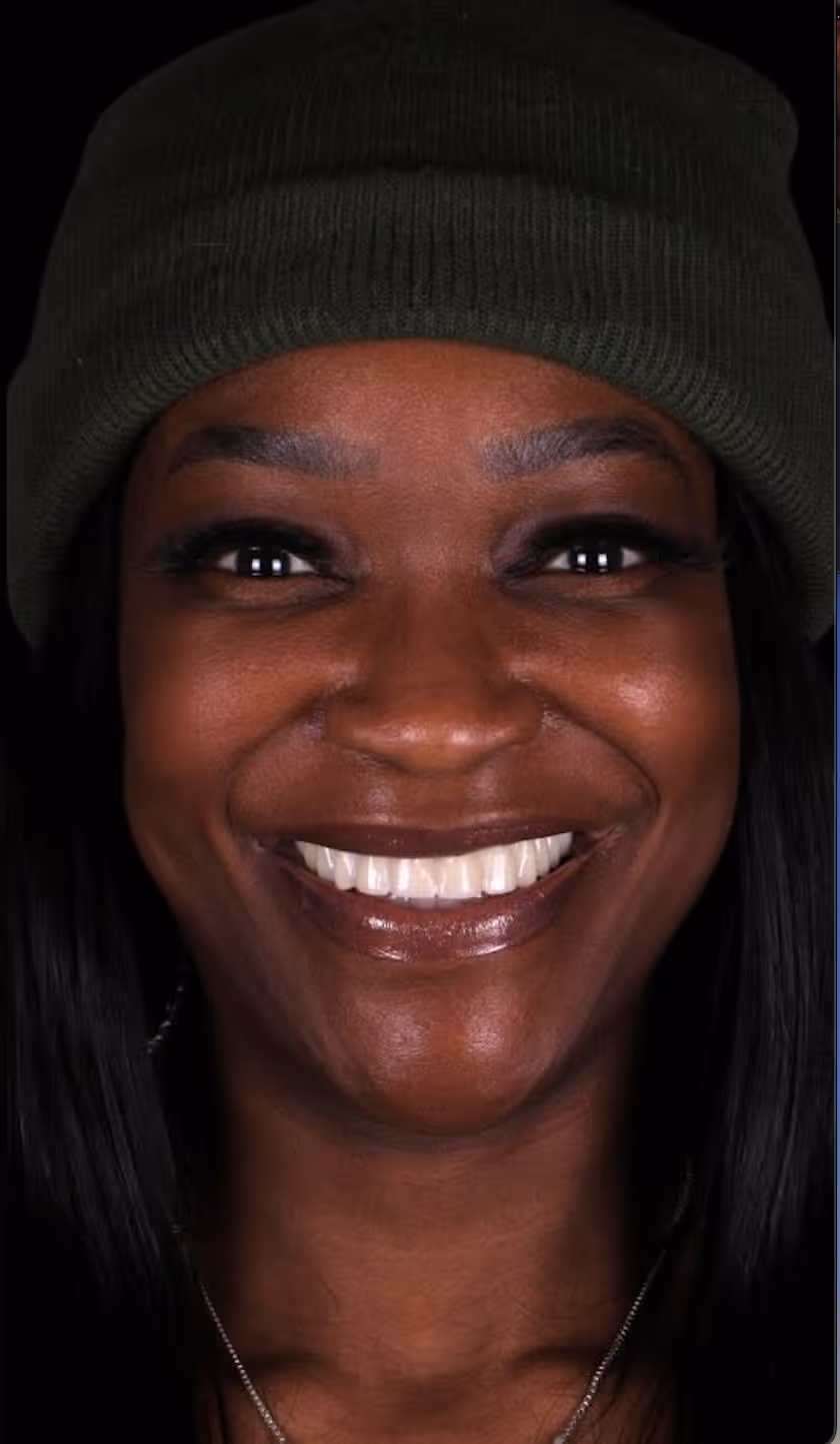 Close-up of a smiling woman wearing a dark green knit beanie and a necklace.