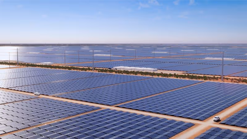 Large solar farm with rows of solar panels under a blue sky, two vehicles on dirt roads between panels, and wind turbines in the background.