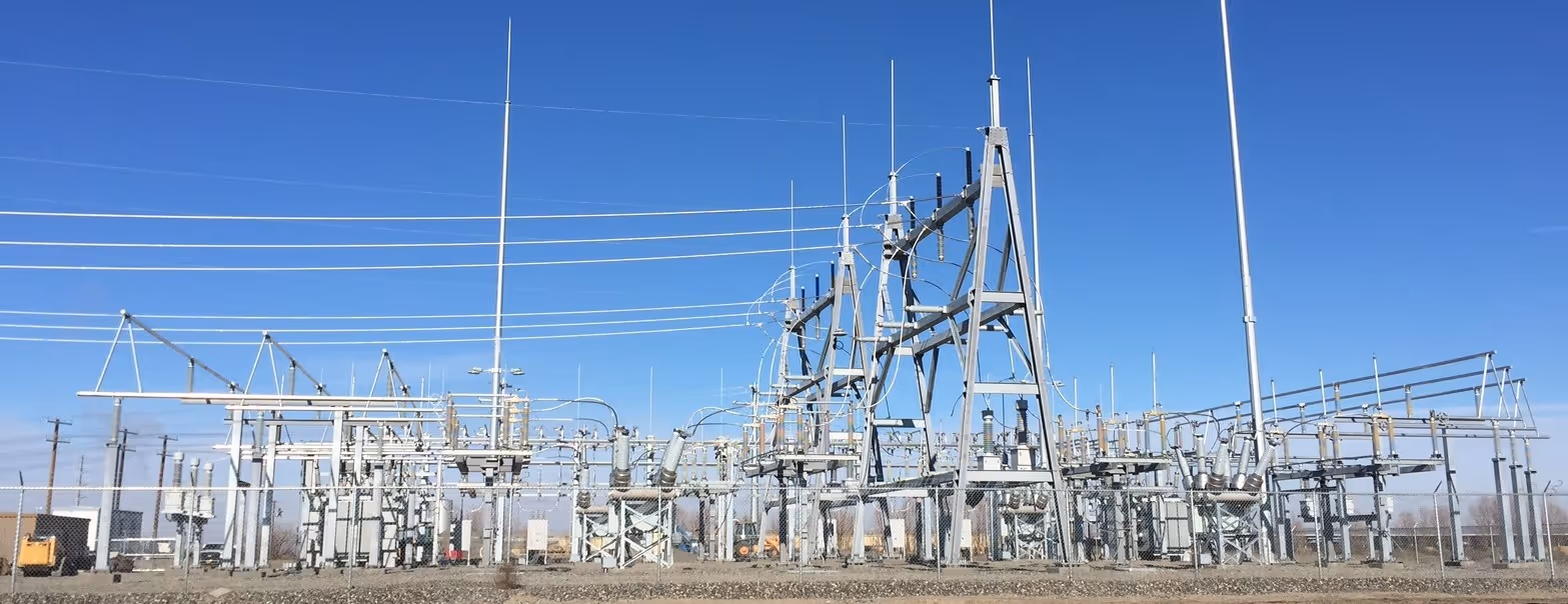 Electrical substation with steel structures, transformers, power lines, and blue sky background.