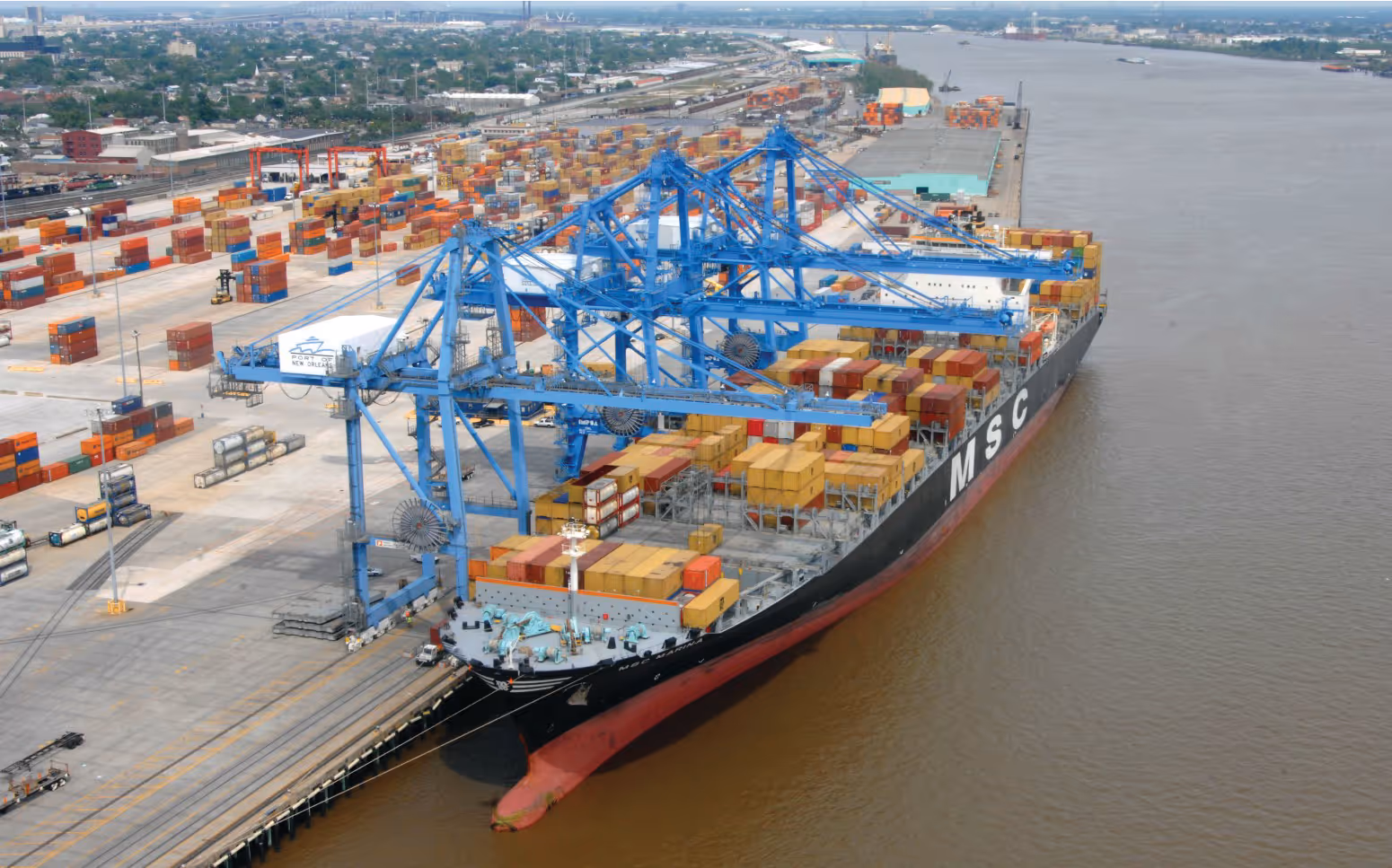 Large container ship docked at Port of New Orleans with blue cranes unloading multicolored shipping containers.