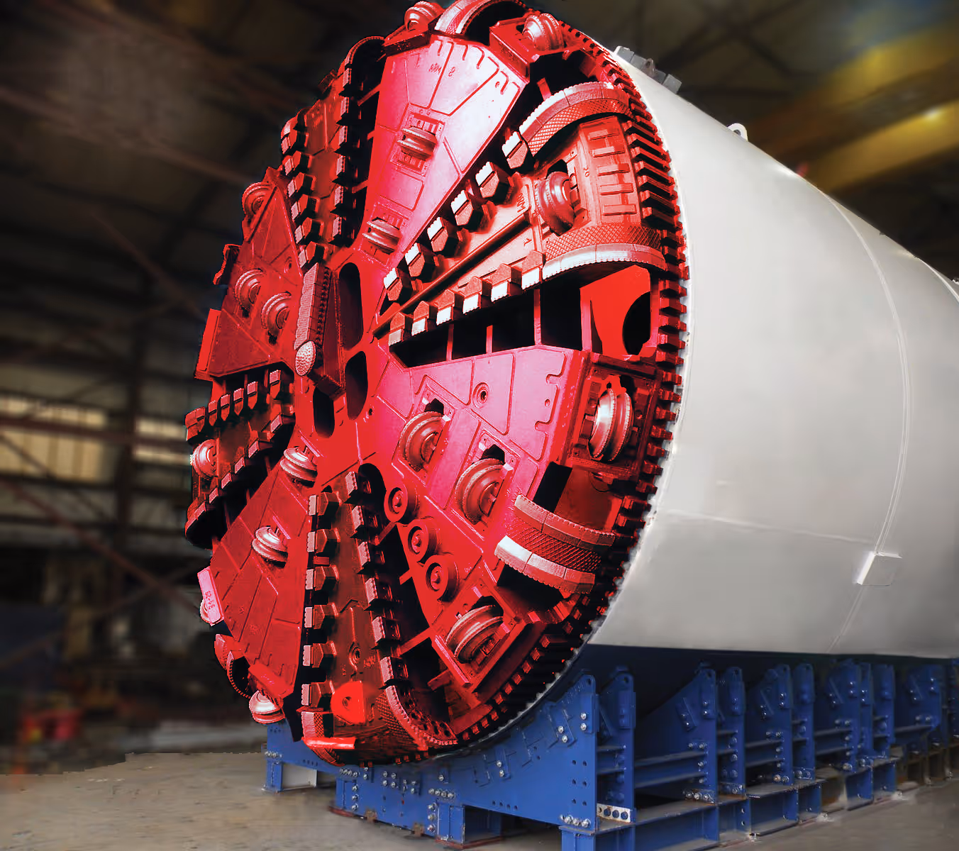 Close-up of a large red tunnel boring machine head inside an industrial warehouse.