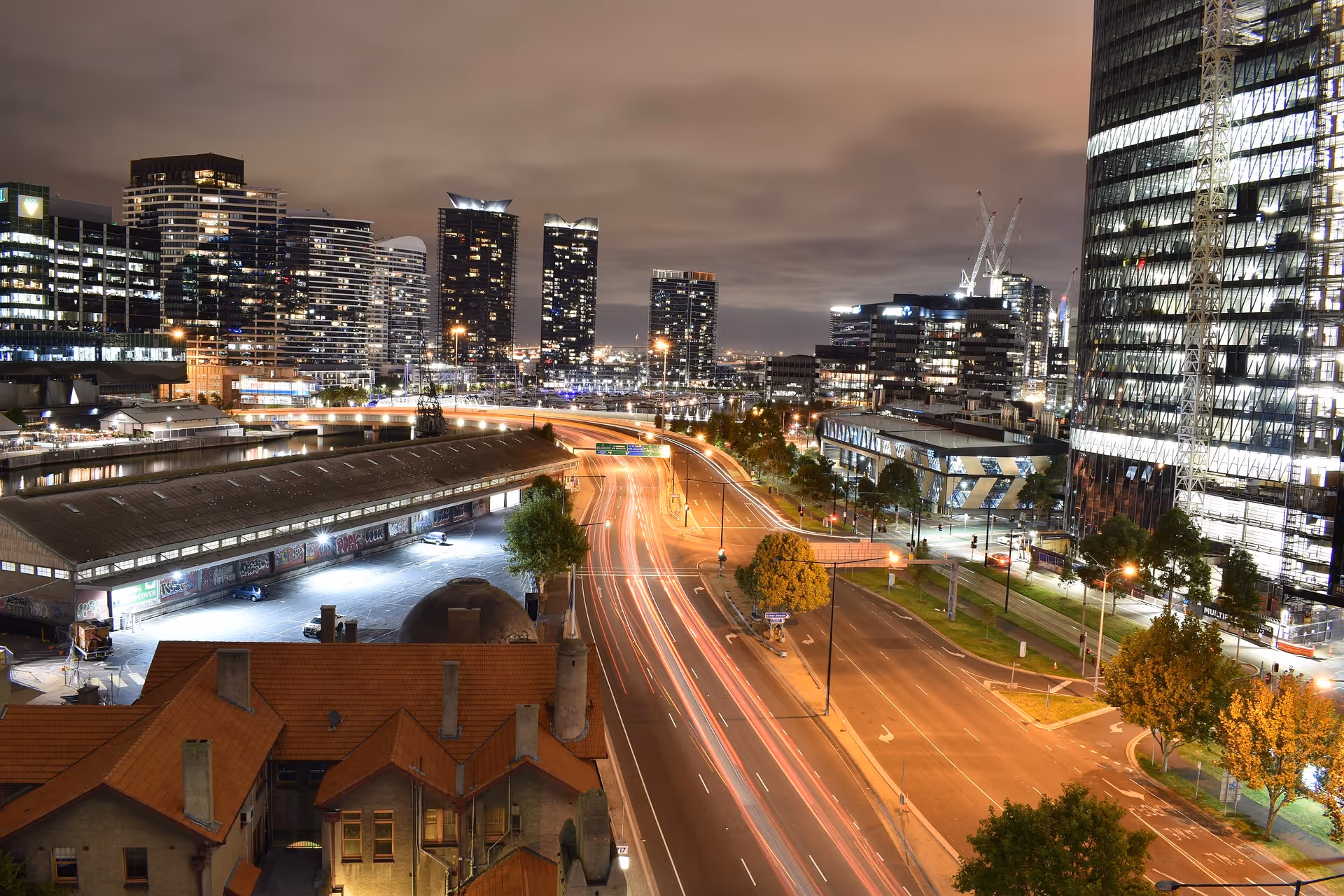 Nighttime cityscape with illuminated skyscrapers, a busy highway with light trails from vehicles, and lit buildings in the foreground.