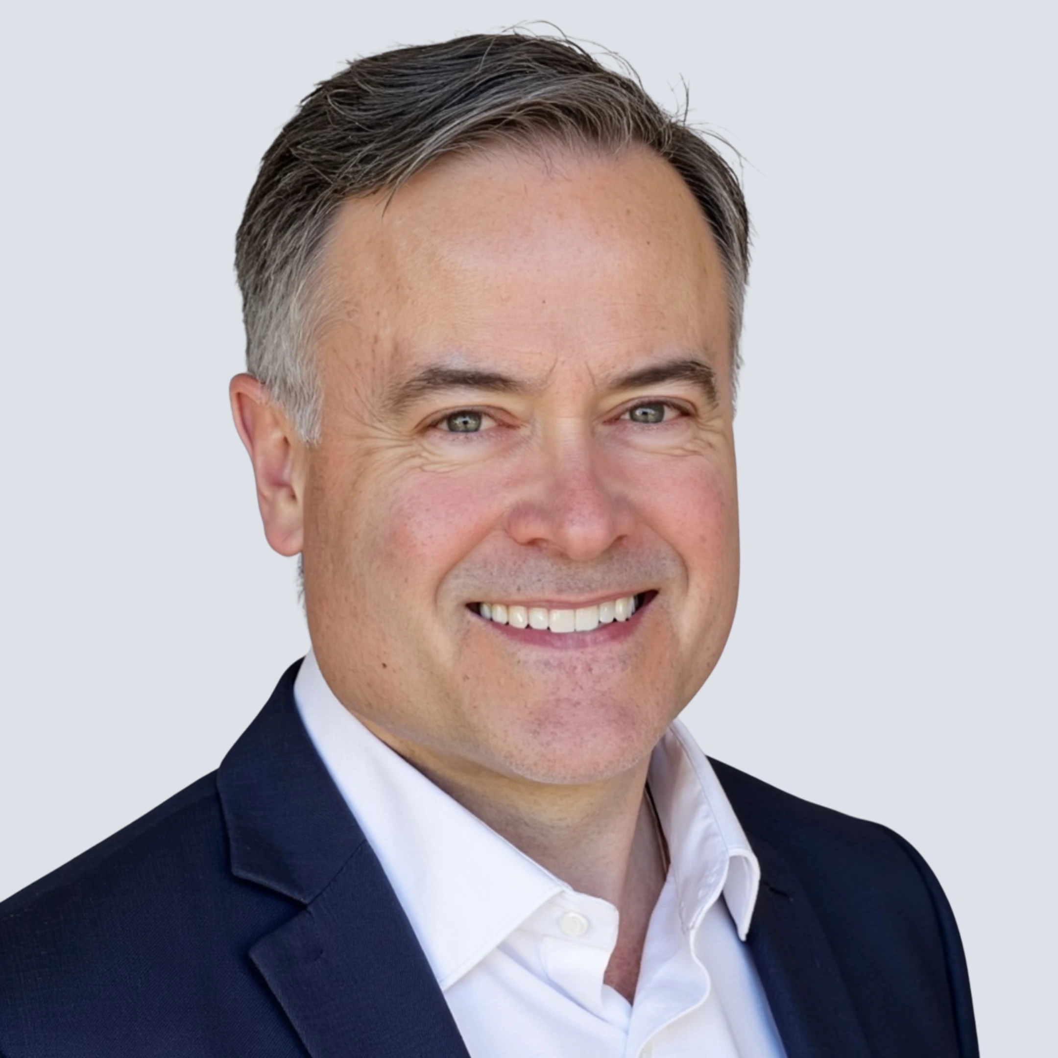 Professional headshot of a middle-aged man wearing a dark suit, white shirt, and striped tie, smiling slightly against a plain light background.