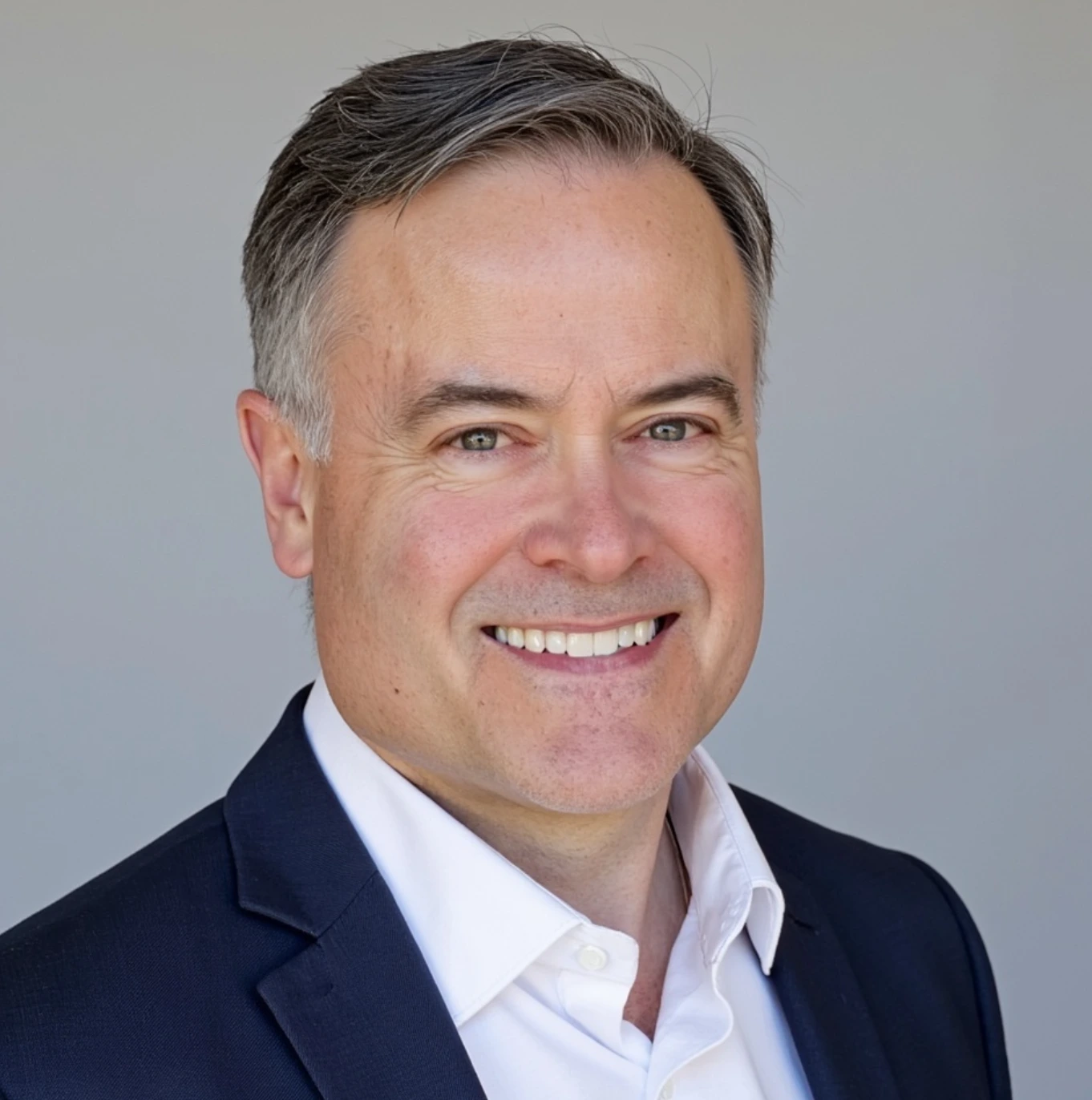 Professional headshot of a middle-aged man wearing a dark suit, white shirt, and striped tie, smiling slightly against a plain light background.