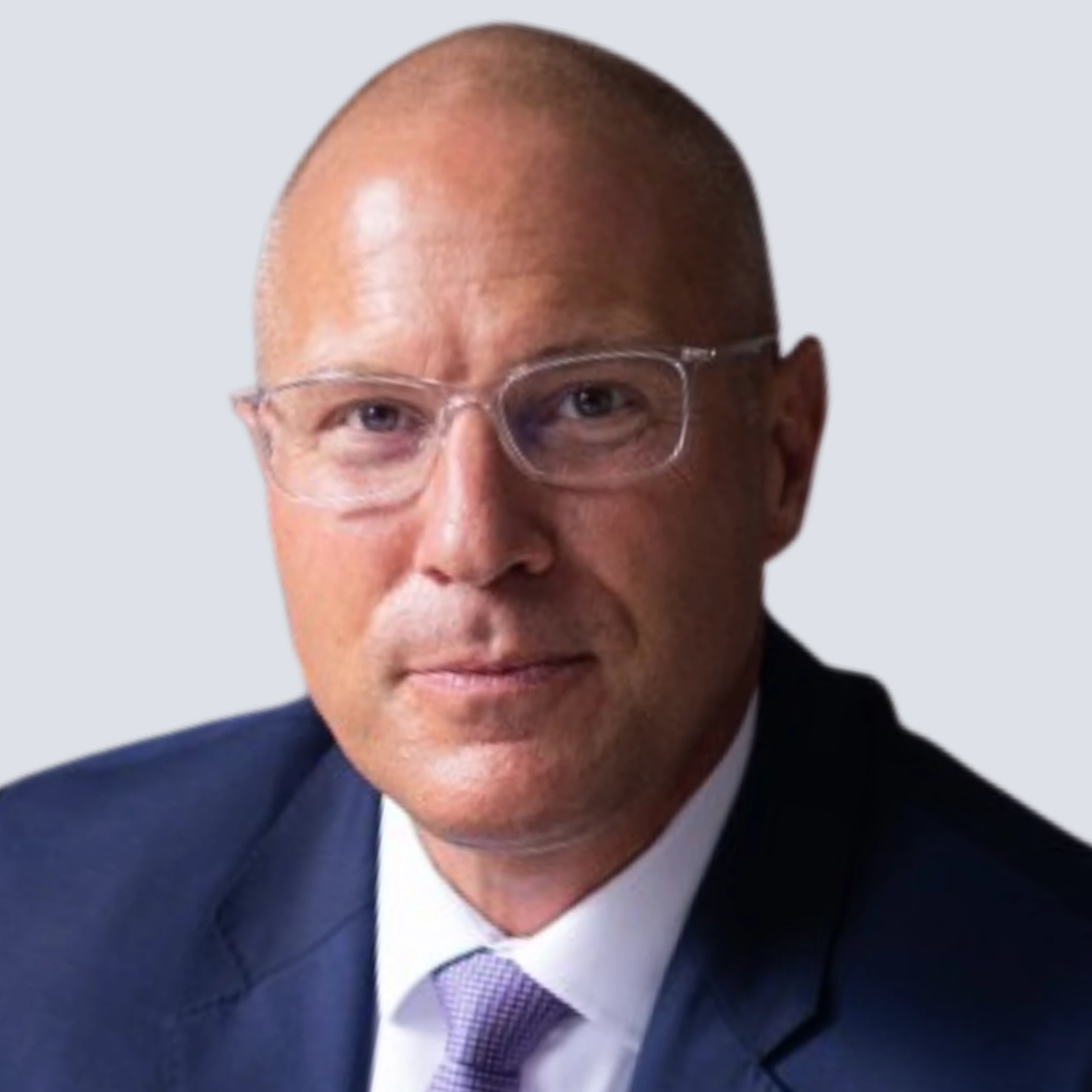 Middle-aged man with glasses wearing a dark suit and white shirt against a plain gray background.