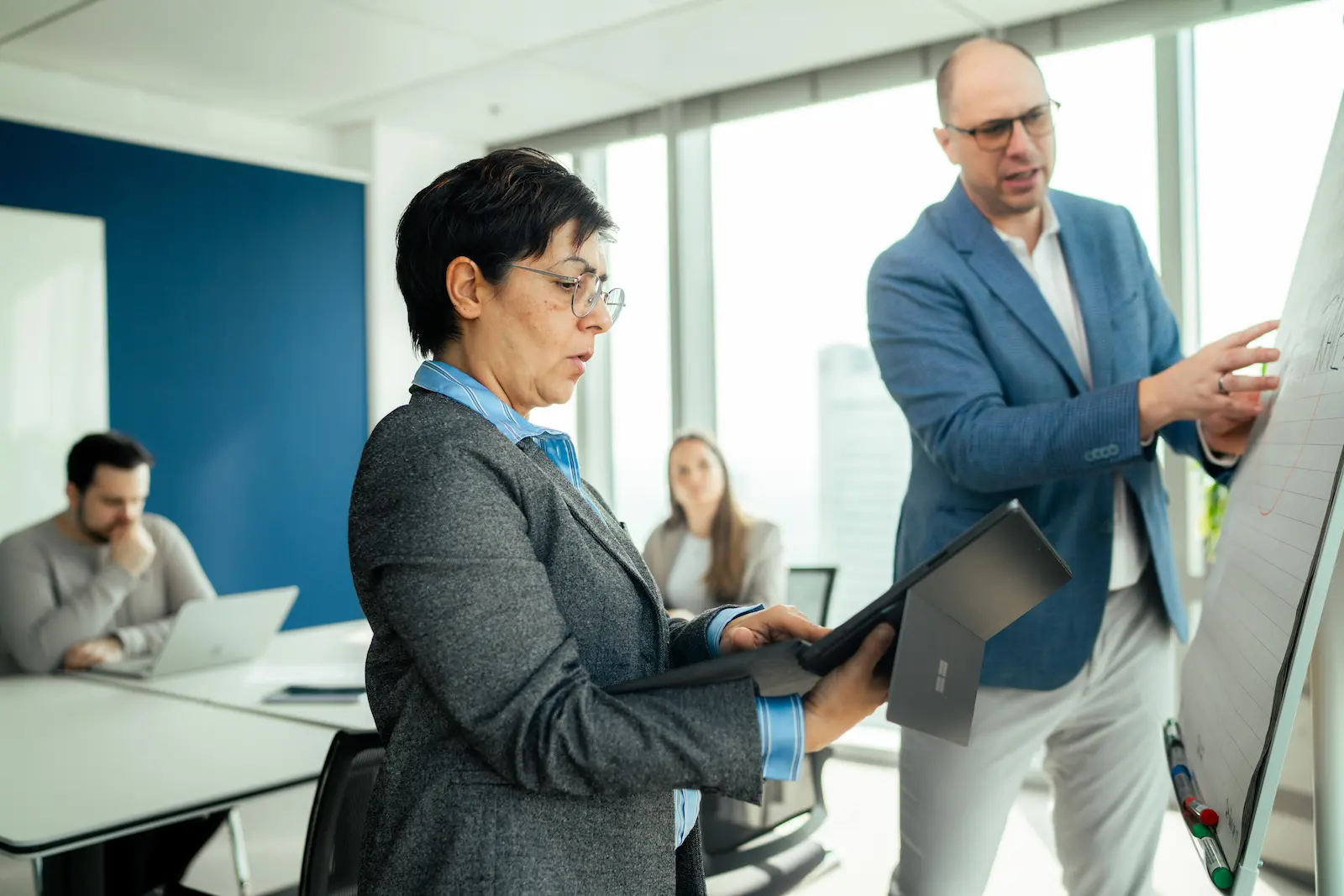 Zwei berufstätige Personen diskutieren während einer Präsentation vor einem Whiteboard in einem modernen Büro.