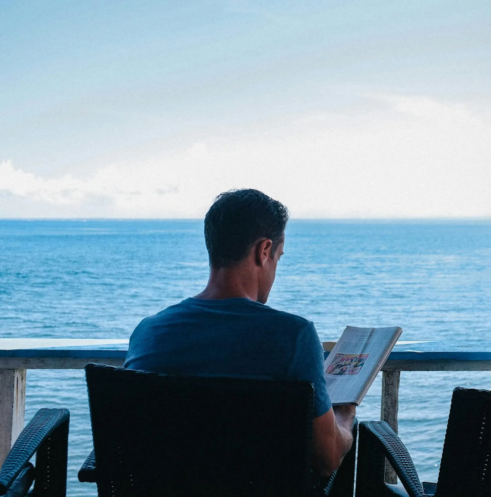 Mann sitzt auf Balkon mit Meerblick