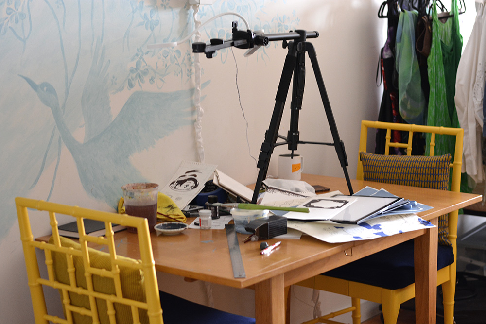 What the table usually looks like. The image depicts a messy table filled with papers as well as a camera tripod on it.