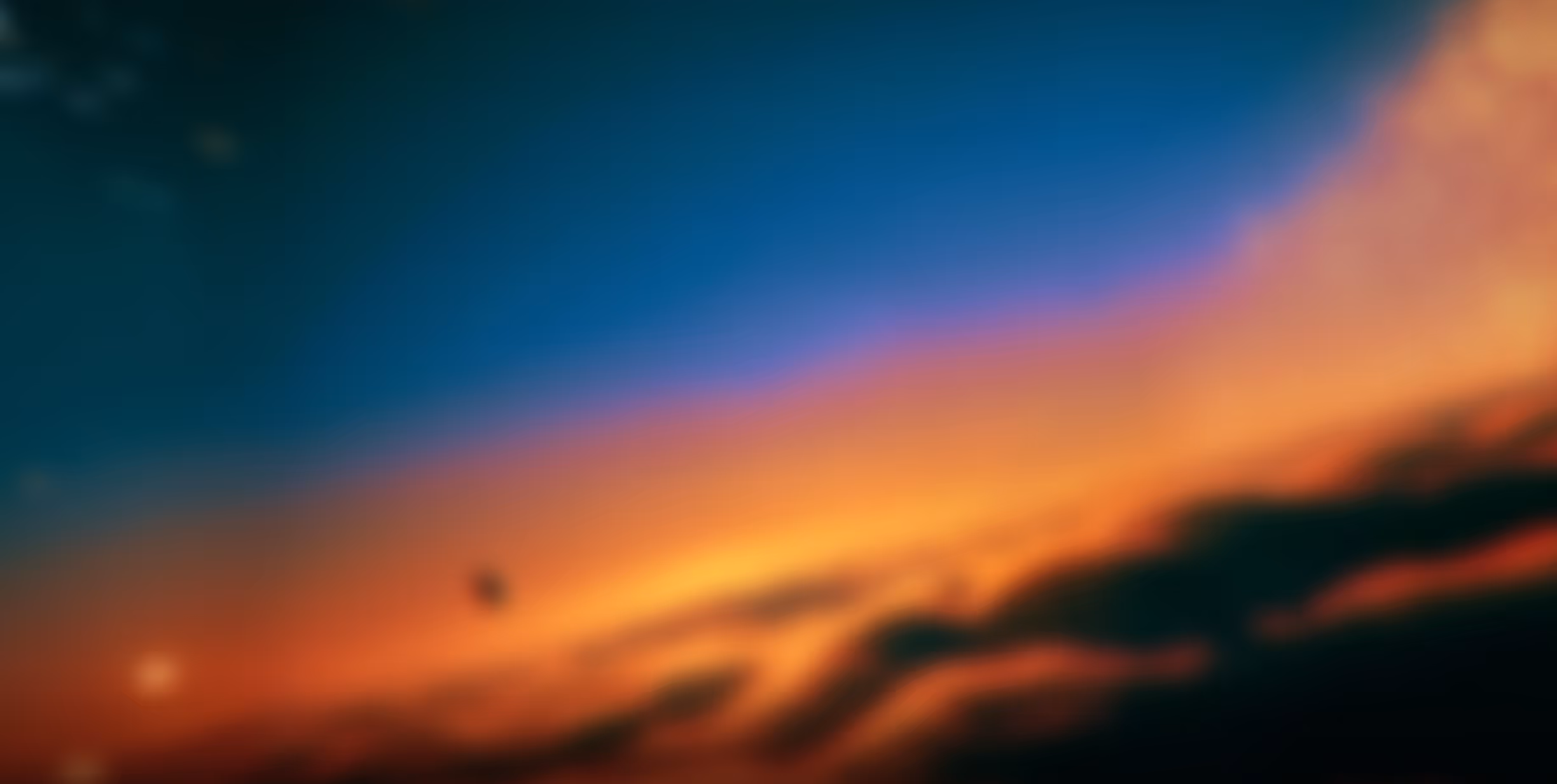 Blurry sky at sunset with gradient colors from dark blue to orange and soft cloud shapes.