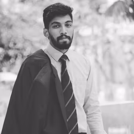 Young man in dress shirt and tie holding a jacket over his shoulder looking at the camera in an outdoor setting.