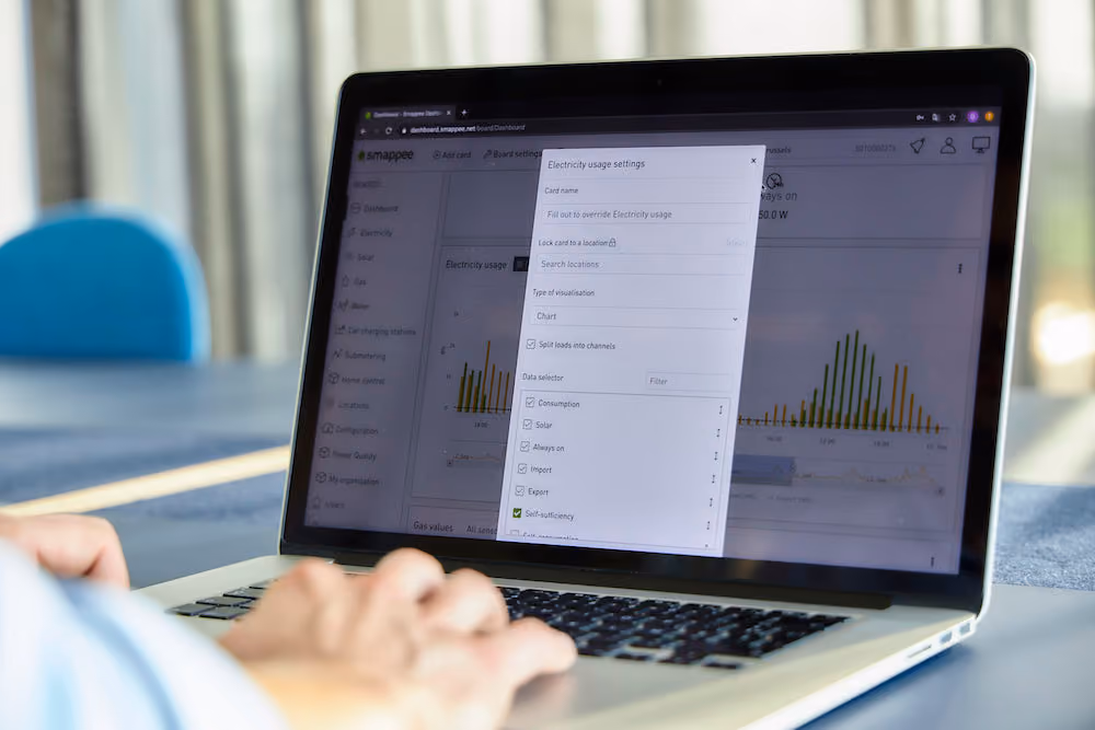 Iemand bedient een laptop met op het scherm een dashboard voor energiebeheer met instellingen voor elektriciteitsverbruik, inclusief opties zoals verbruik, zon, altijd aan, import, export en zelfvoorziening.