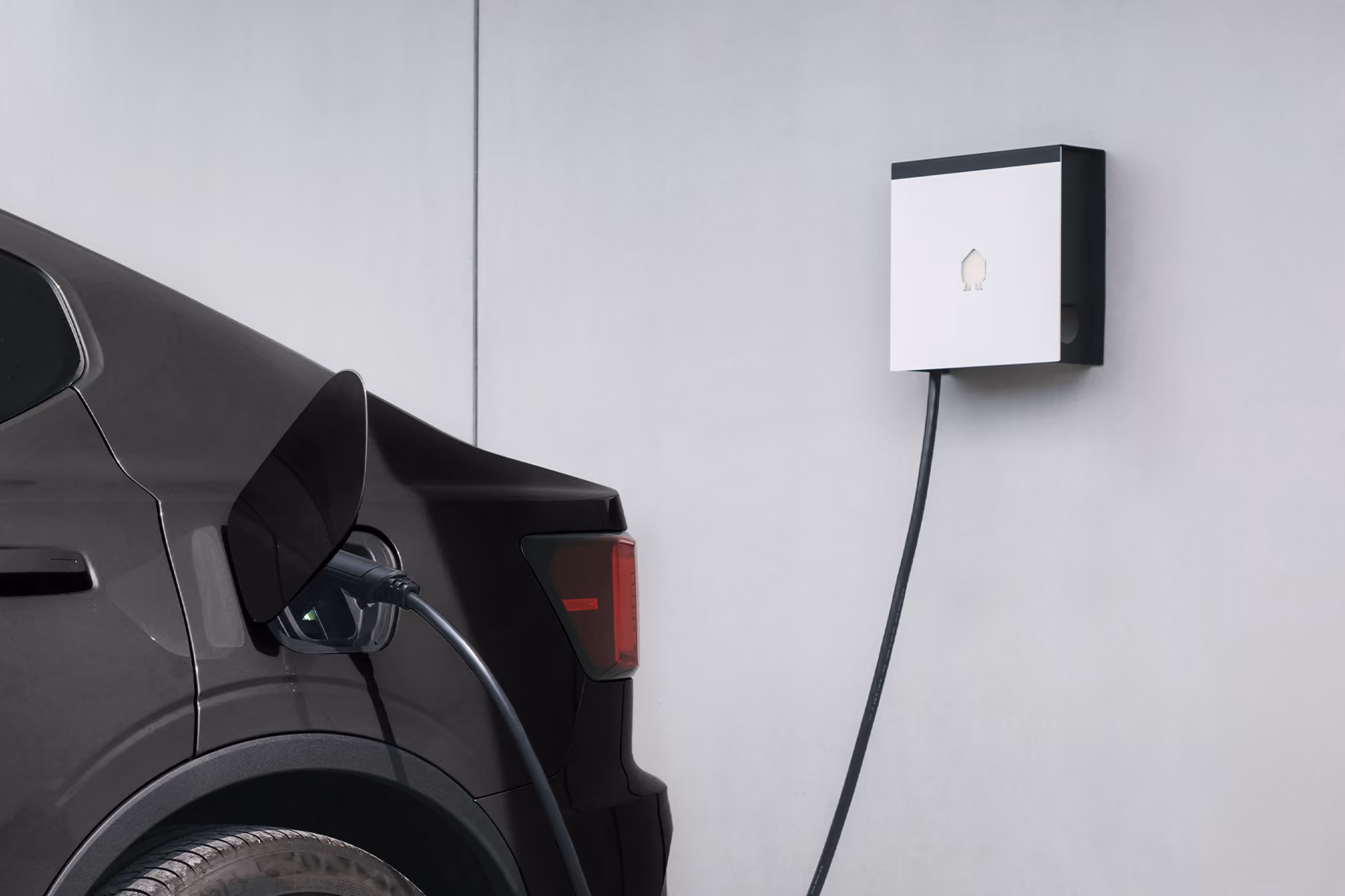 Elektrische auto met oplaadkabel aangesloten op een wandladepunt aan een witte muur.