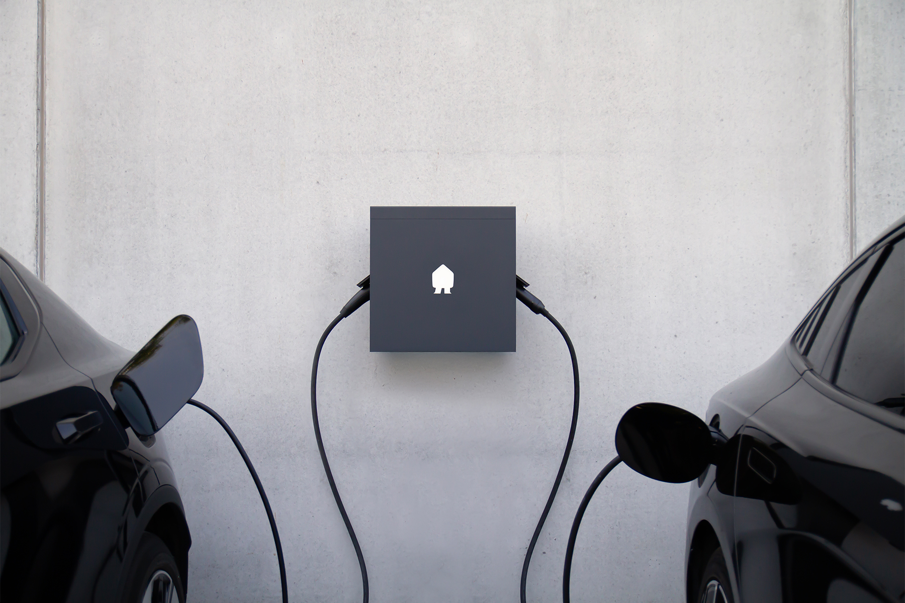 Twee elektrische zwarte auto's die opladen aan een grijs laadstation bevestigd aan een betonnen muur.